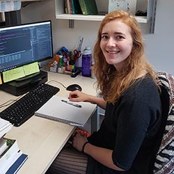 Femme presenting person with strawberry blonde hair sitting at a computer