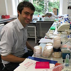 Masculine presenting person with dark hair sits at a lab desk