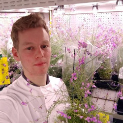 Masculine presenting person with blond hair next to flowers in a lab